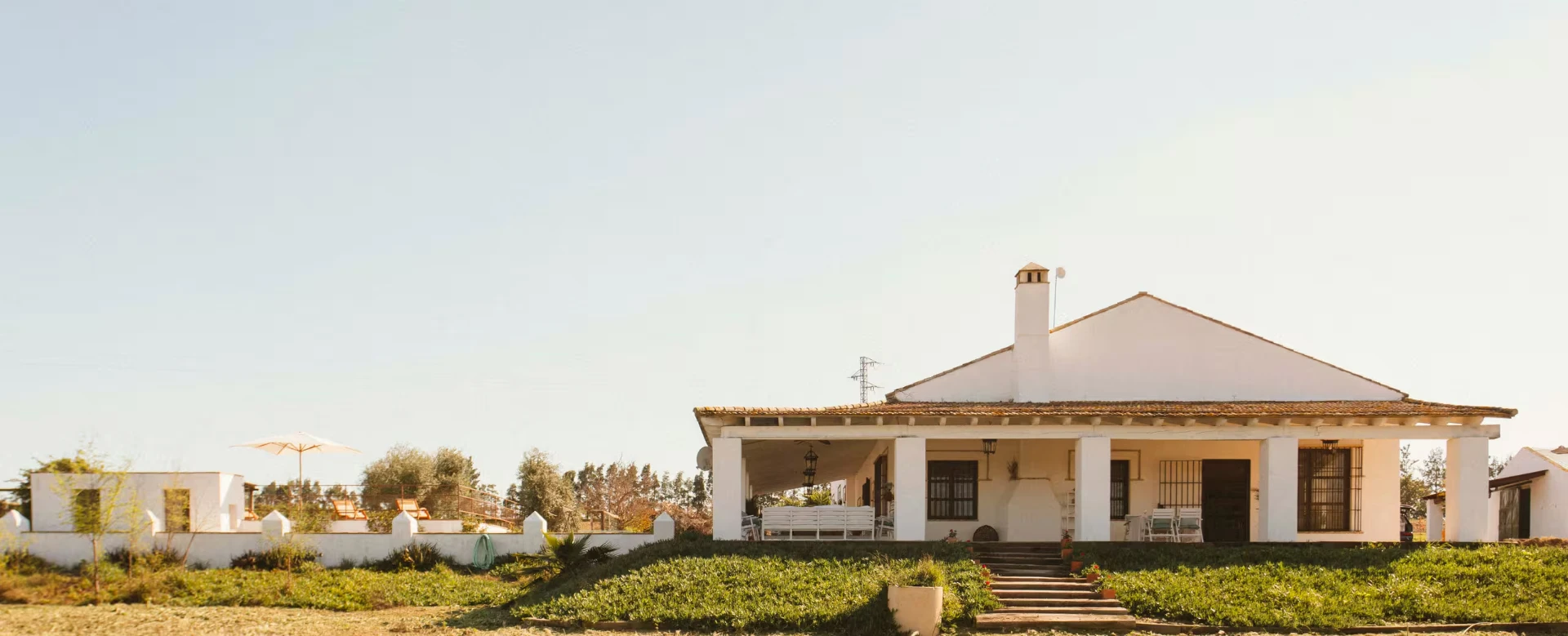 Whitewashed farmhouse with tiled roof and shaded porch among the groves